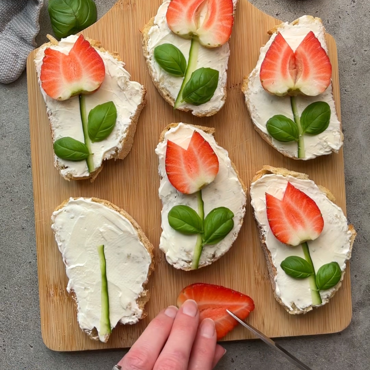 A hand slices a strawberry on a wooden board.