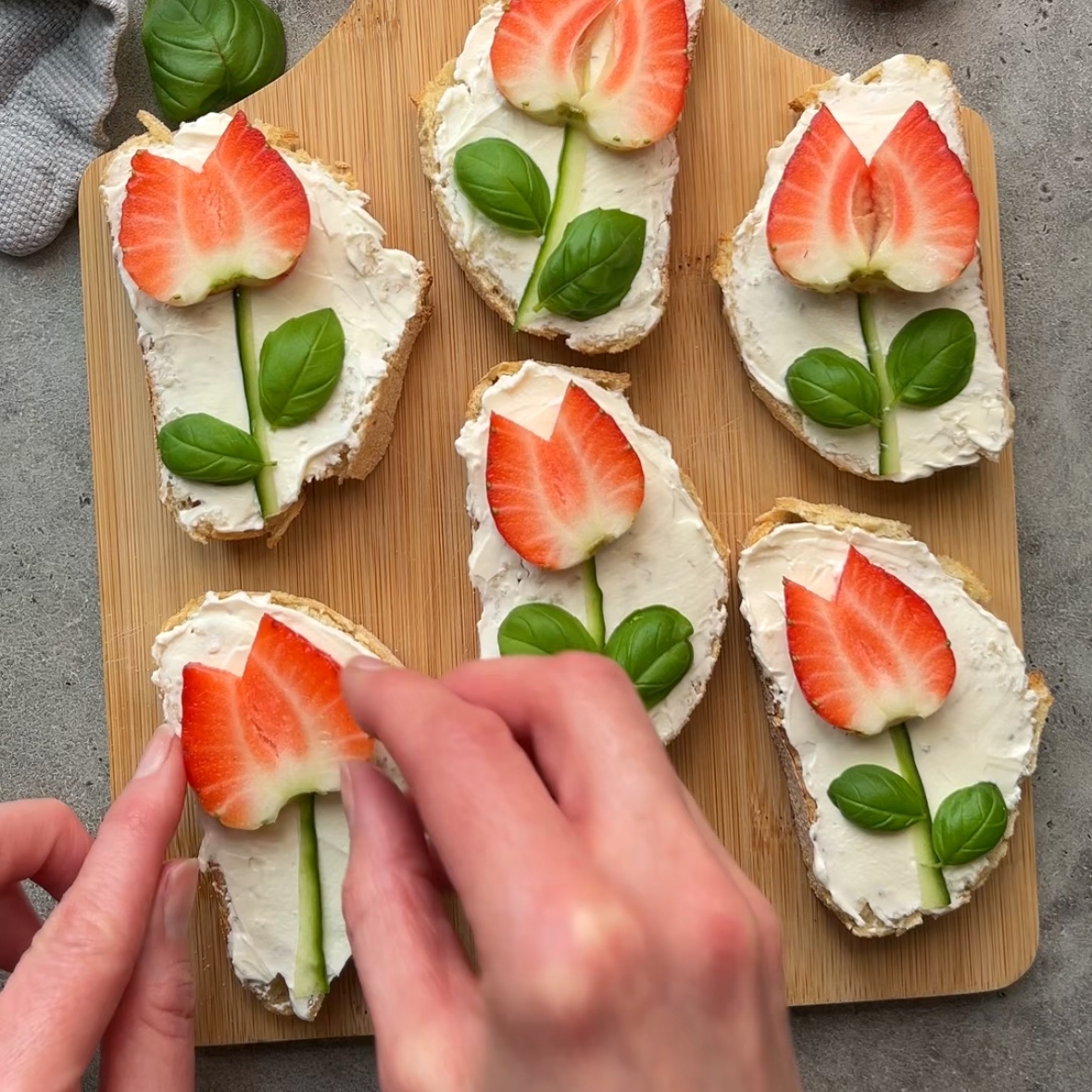 Two hands adjust a strawberry tulip onto a crostini in the foreground.