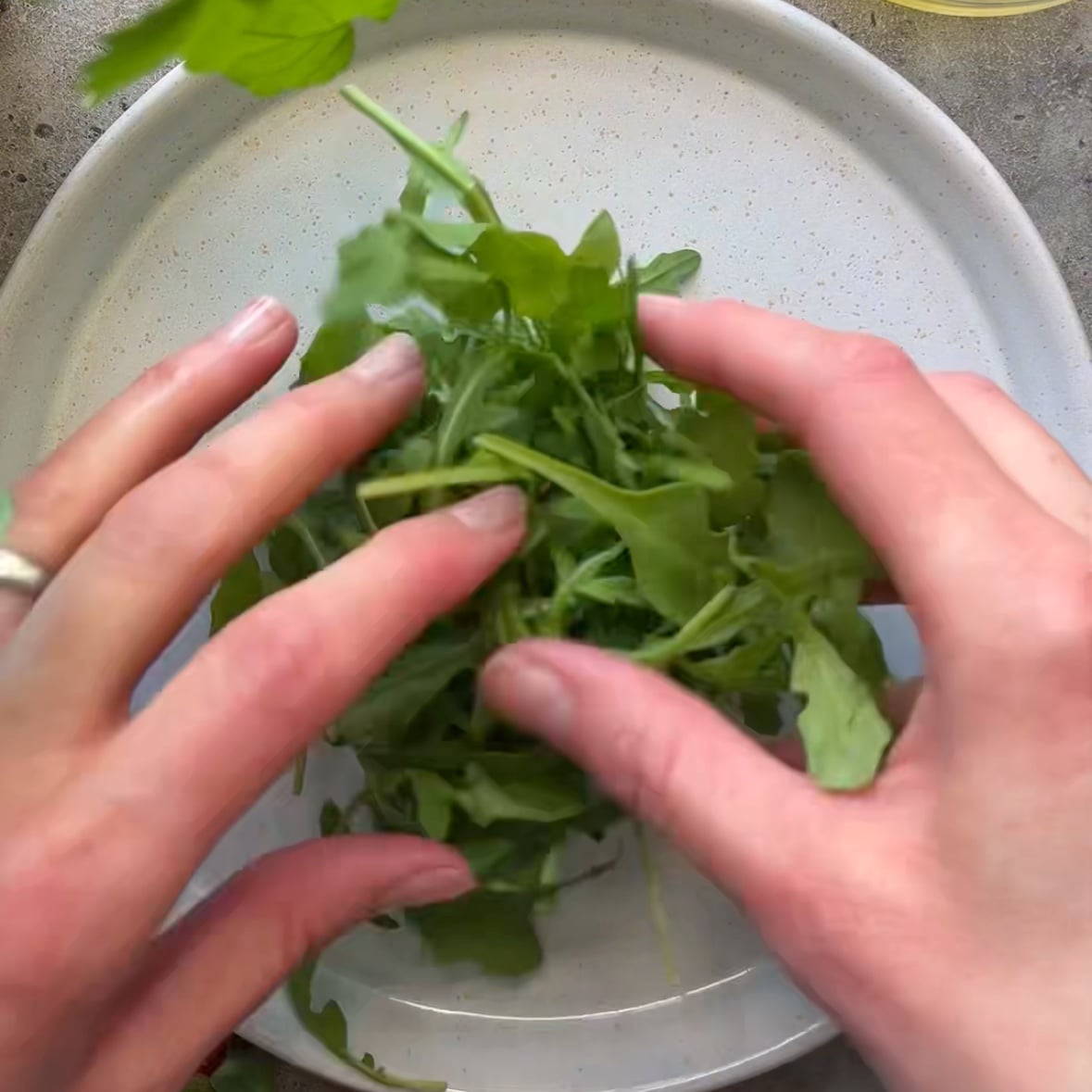 Two hands arrange fresh arugula leaves on a white plate.