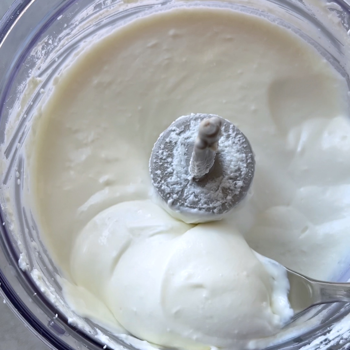 A close-up view of thick, creamy whipped feta being blended in a food processor.