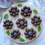 Chocolate Covered Blueberry clusters arranged in a flower shape on a round marble plate, garnished with fresh mint leaves.