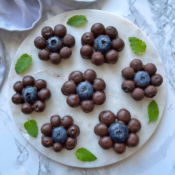 Chocolate Covered Blueberry clusters arranged in a flower shape on a round marble plate, garnished with fresh mint leaves.