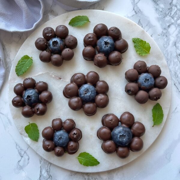 Chocolate Covered Blueberry clusters arranged in a flower shape on a round marble plate, garnished with fresh mint leaves.