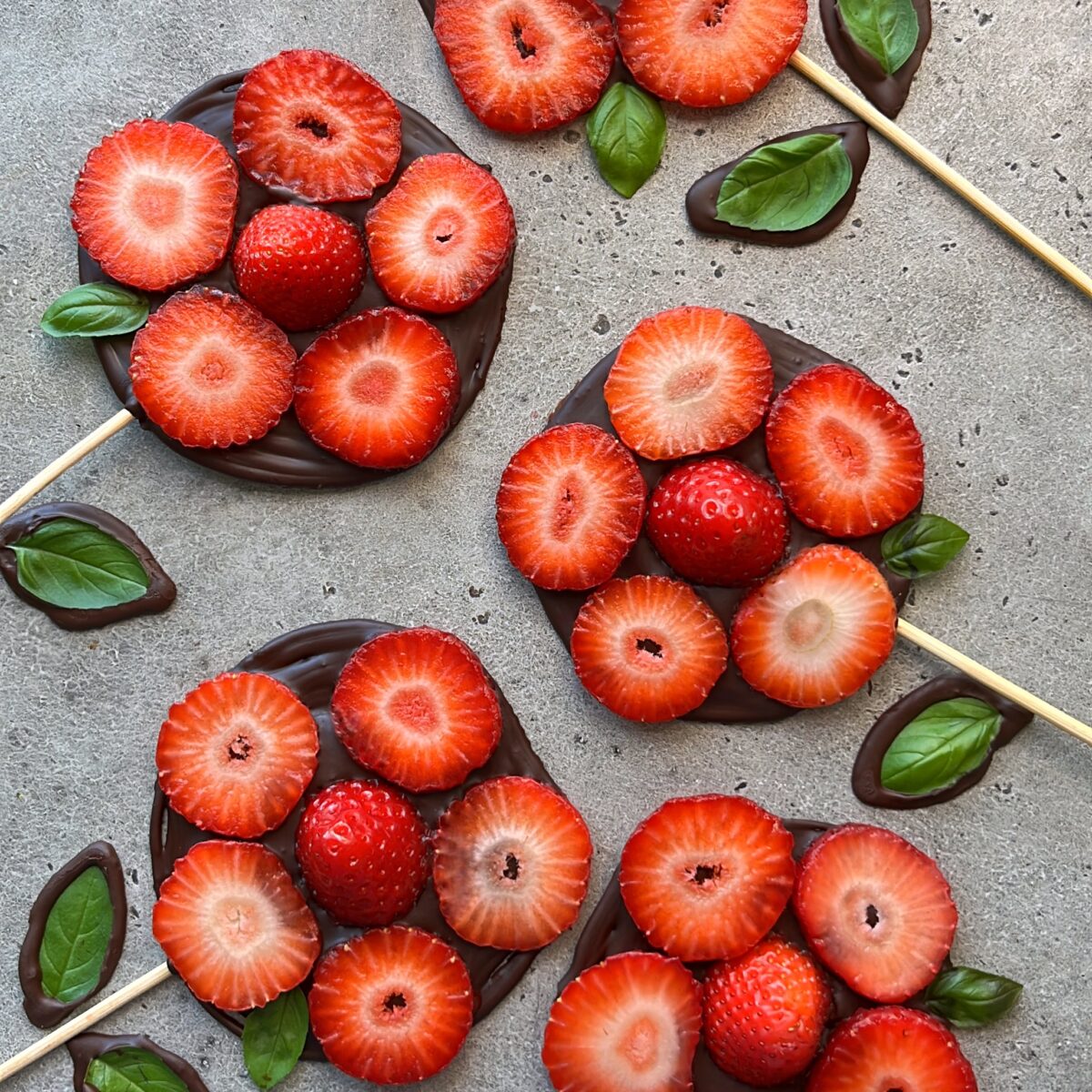 Round chocolate discs topped with sliced strawberries and fresh basil leaves.