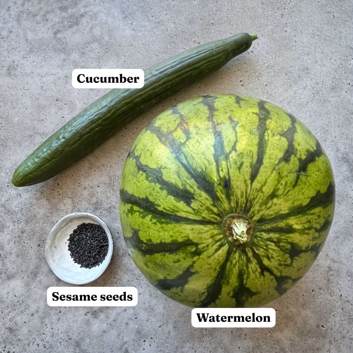 A whole cucumber, a bowl of black sesame seeds, and a whole watermelon.
