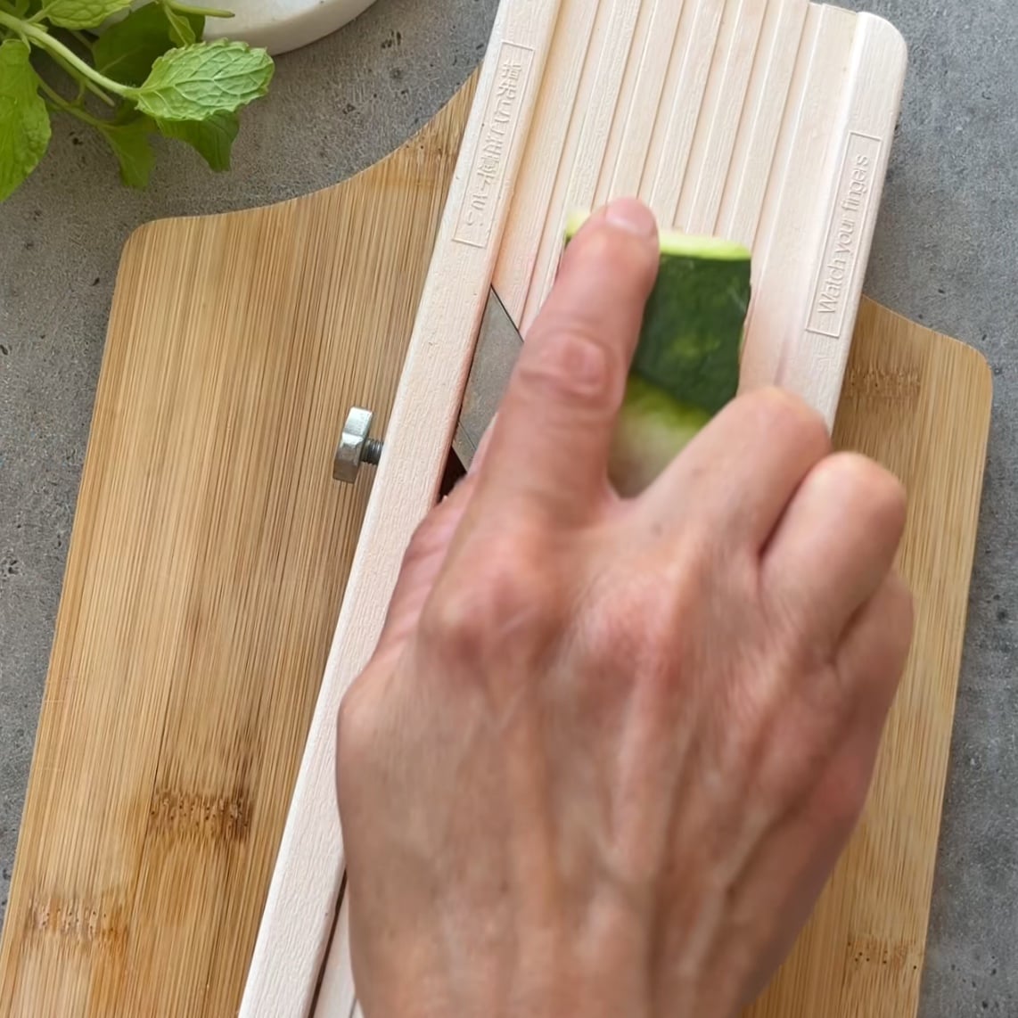 A hand slices a piece of watermelon using a mandoline slicer.