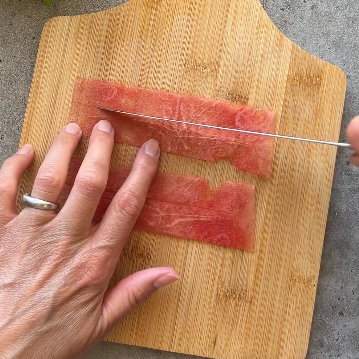 A person slices two rectangular pieces of watermelon in half.