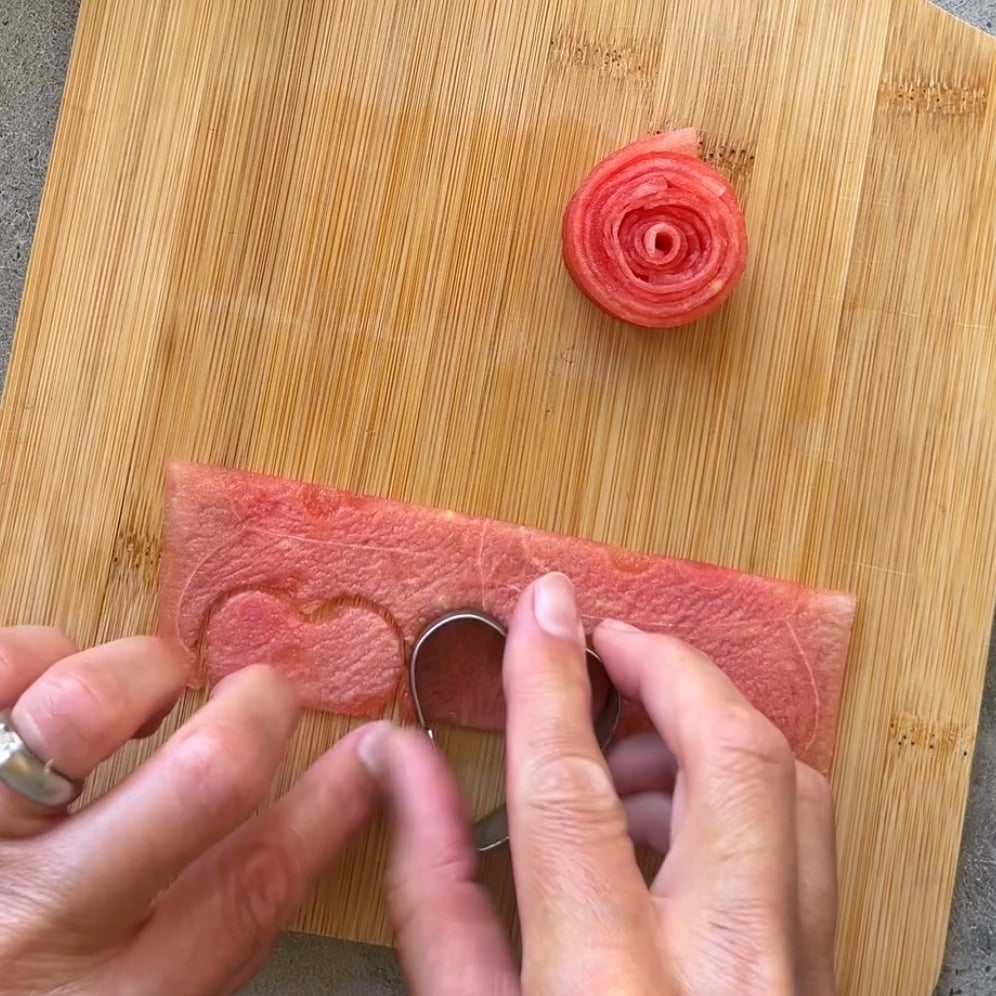 A person uses a heart shaped metal cutter on a piece of watermelon.