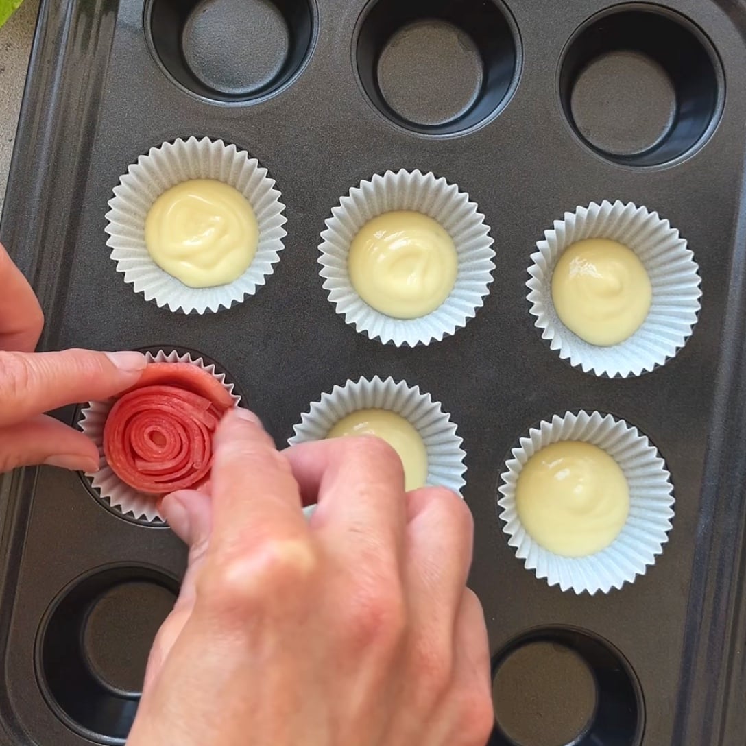 A person places a rolled watermelon rose into a muffin tin lined with white chocolate and paper cups.