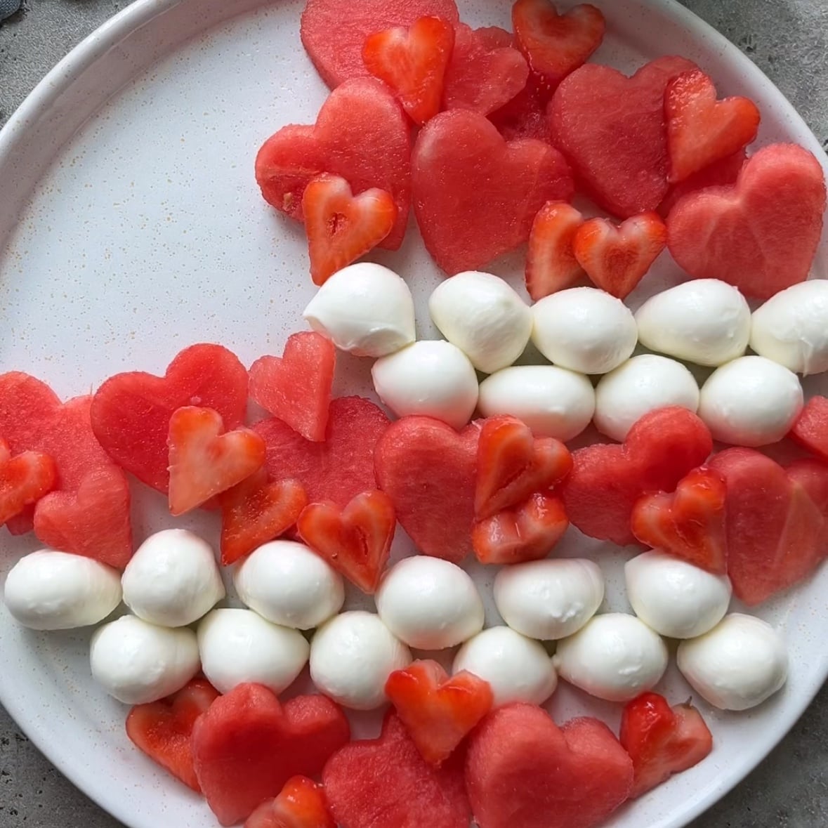 Preparing a 4th of July salad with strips of strawberry and watermelon, as well as bocconcini strips. 