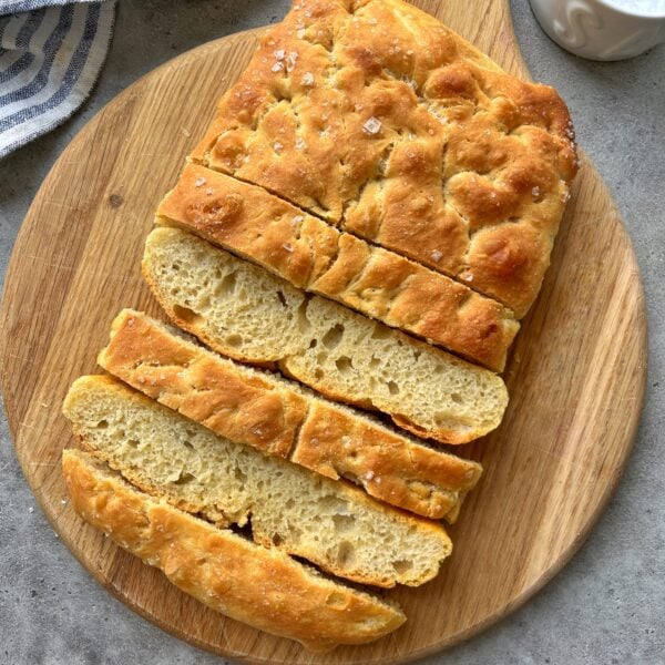 A sliced loaf of focaccia bread with a golden crust, displayed on a round wooden cutting board.