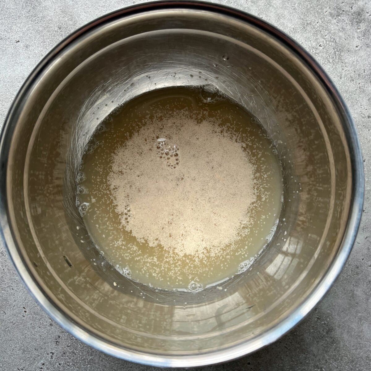 A metal bowl containing water with yeast dissolving on the surface.