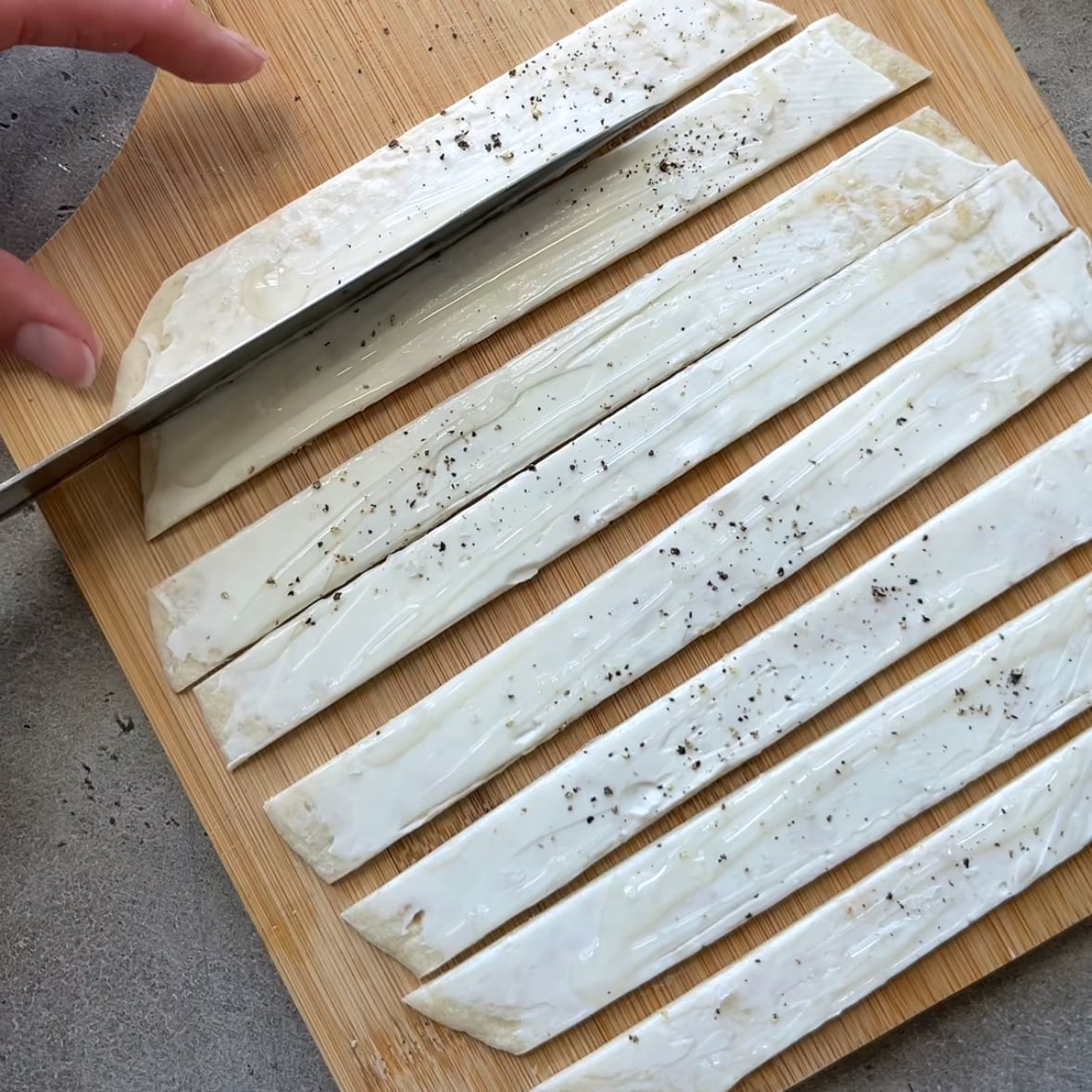 A hand is slicing a tortilla into 8 strips.
