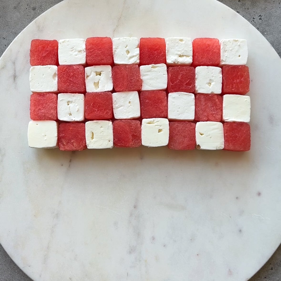 Watermelon and feta cubes are arranged in four rows in a chessboard pattern.