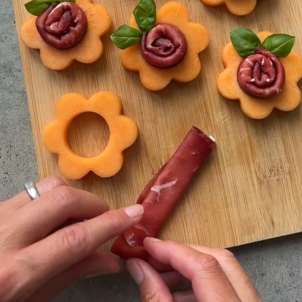 Hands roll a slice of cured meat.