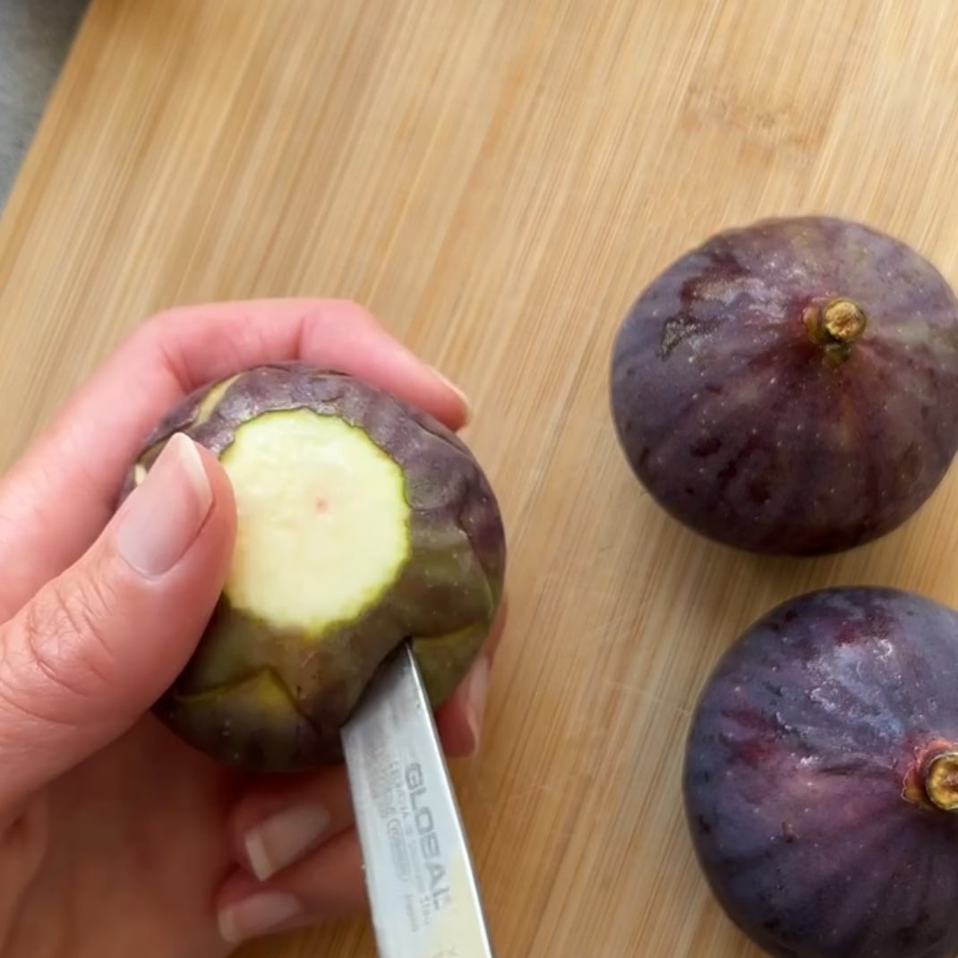 A hand uses a knife to cut the center of a fig into a zig zag.