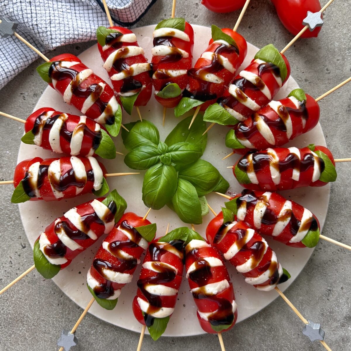 Tomato mozzaarella skewers arranged on a marble platter topped with balsamic glaze. They are ready to eat.