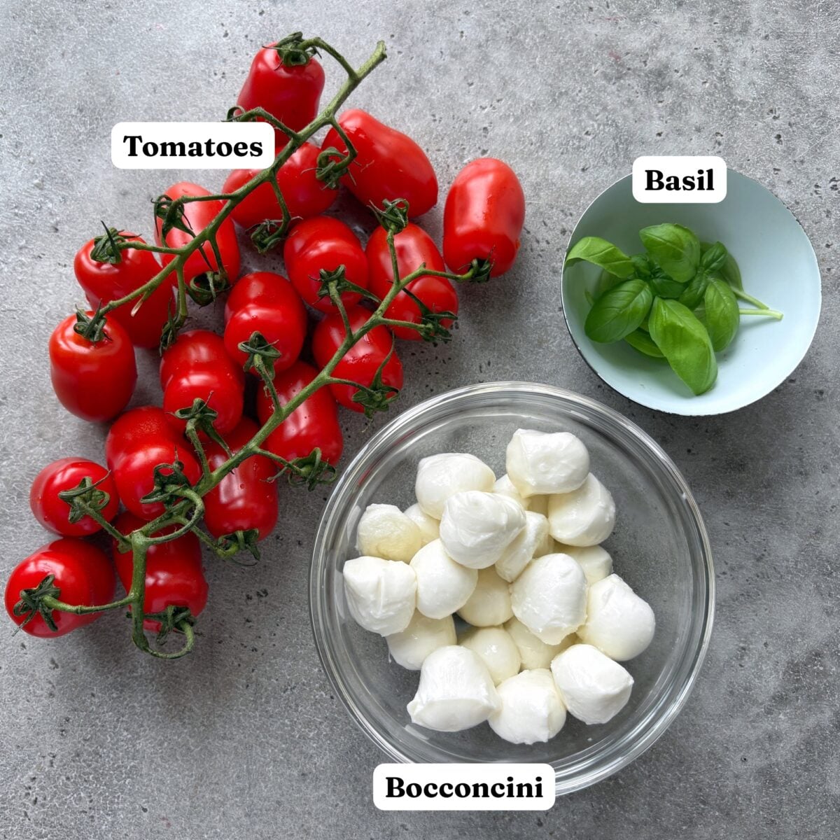 Ingredients for Tomato Mozzarella Skewers featuring a bowl of bocconcini, fresh basil, and San Marzano tomatoes.