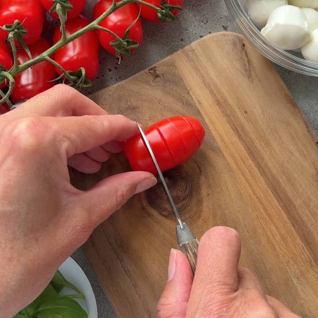 A person slices a tomato 3/4 of the way through to prepare for Tomato Mozzarella Skewers.