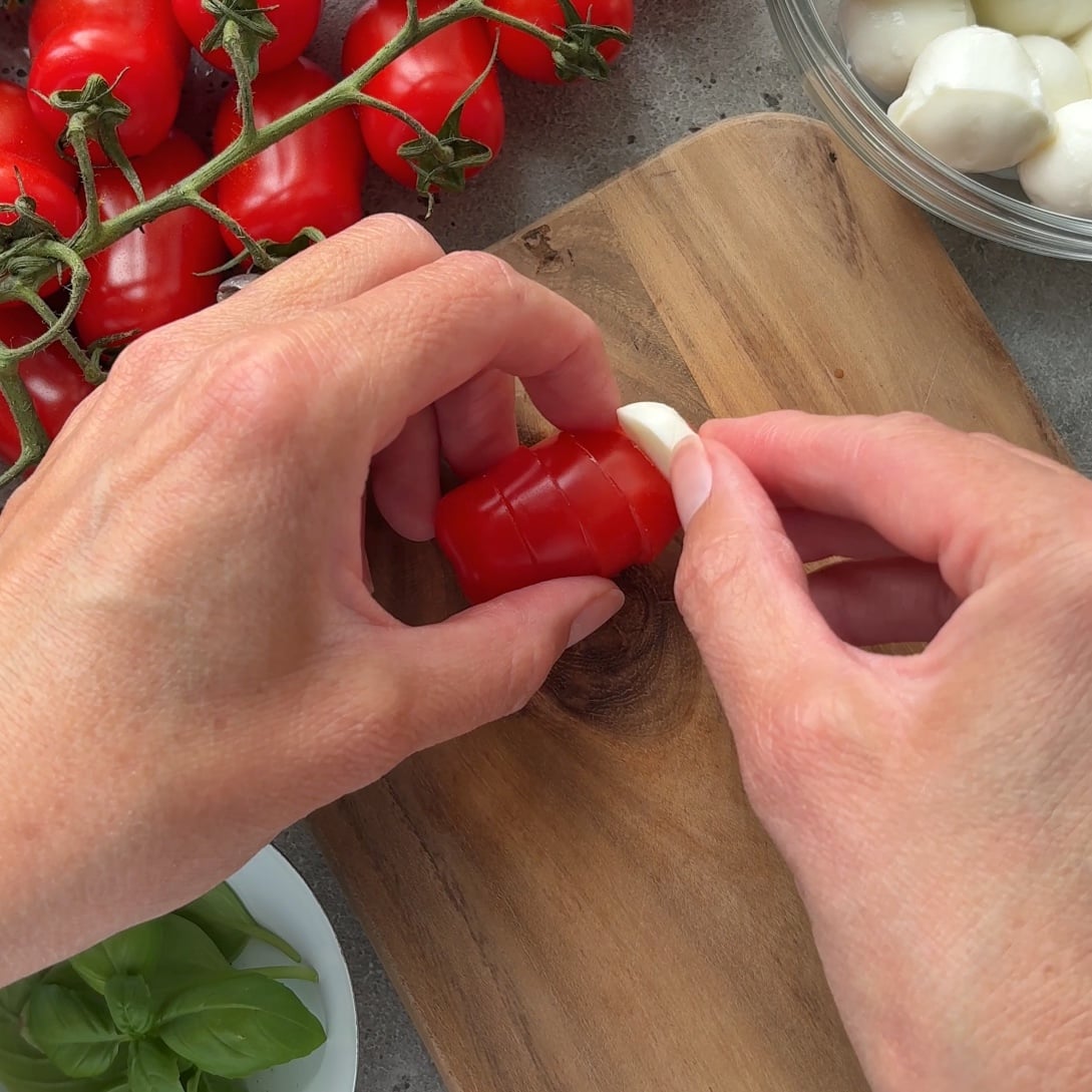 A person inserts a bocconcini slice into the sliced tomato. 