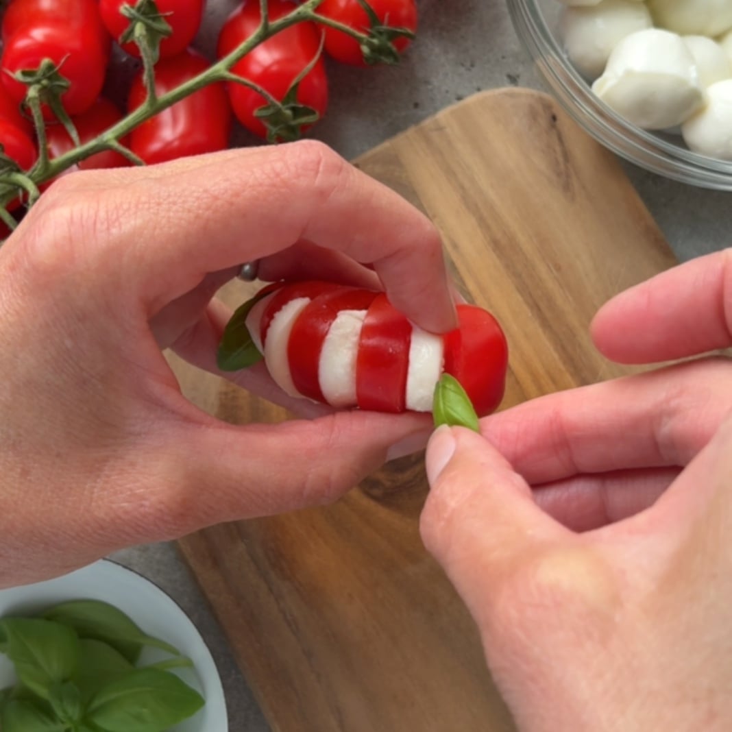 A person tops a fresh basil leaf into each Tomato Mozzarella appetizer.