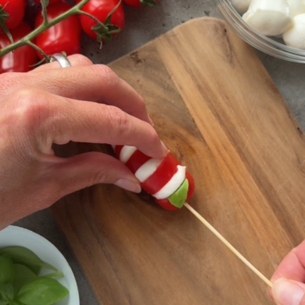 A hand pushes a skewer through a tomato and mozzarella appetizer.