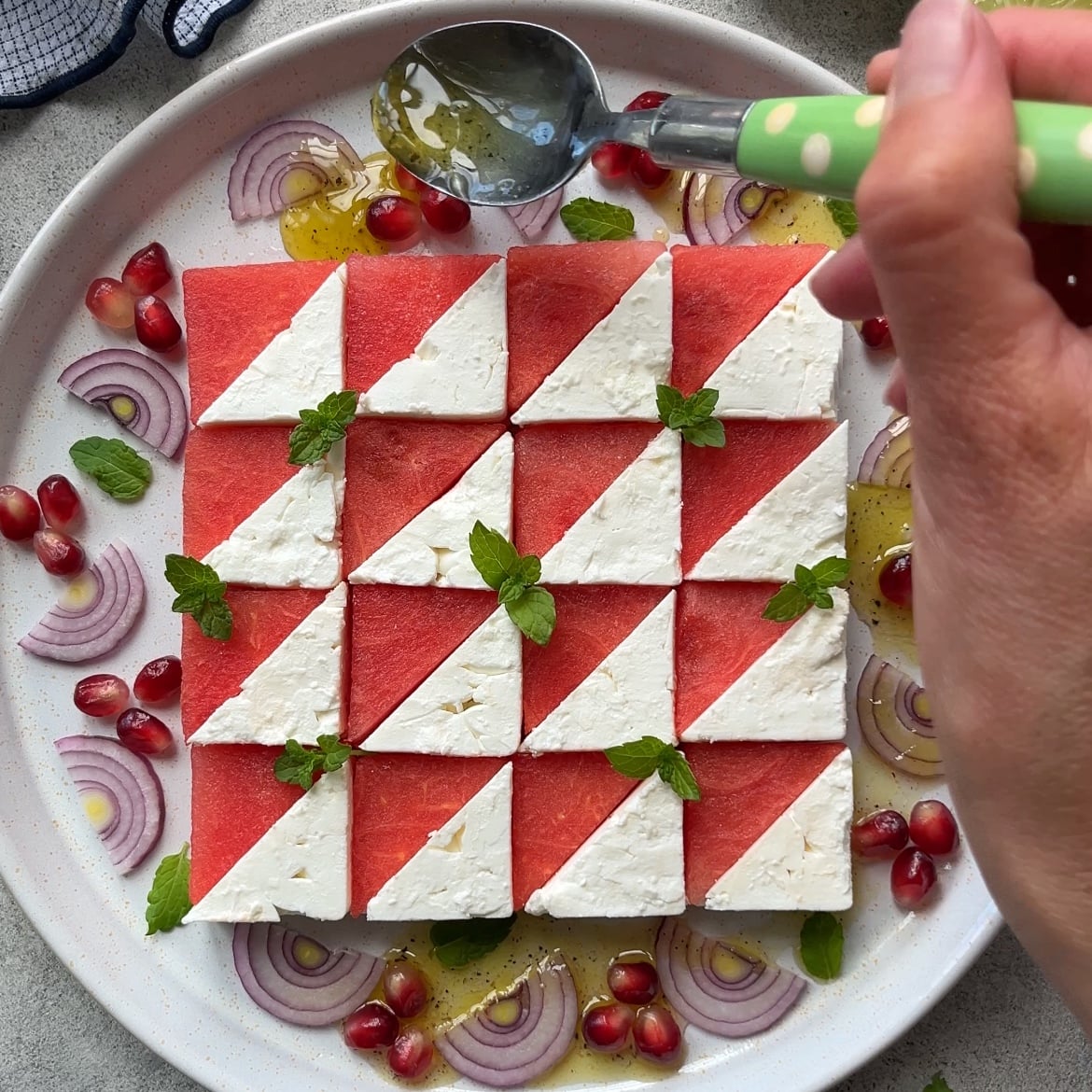 A hand spoons dressing over a plate of Watermelon Mint Salad.