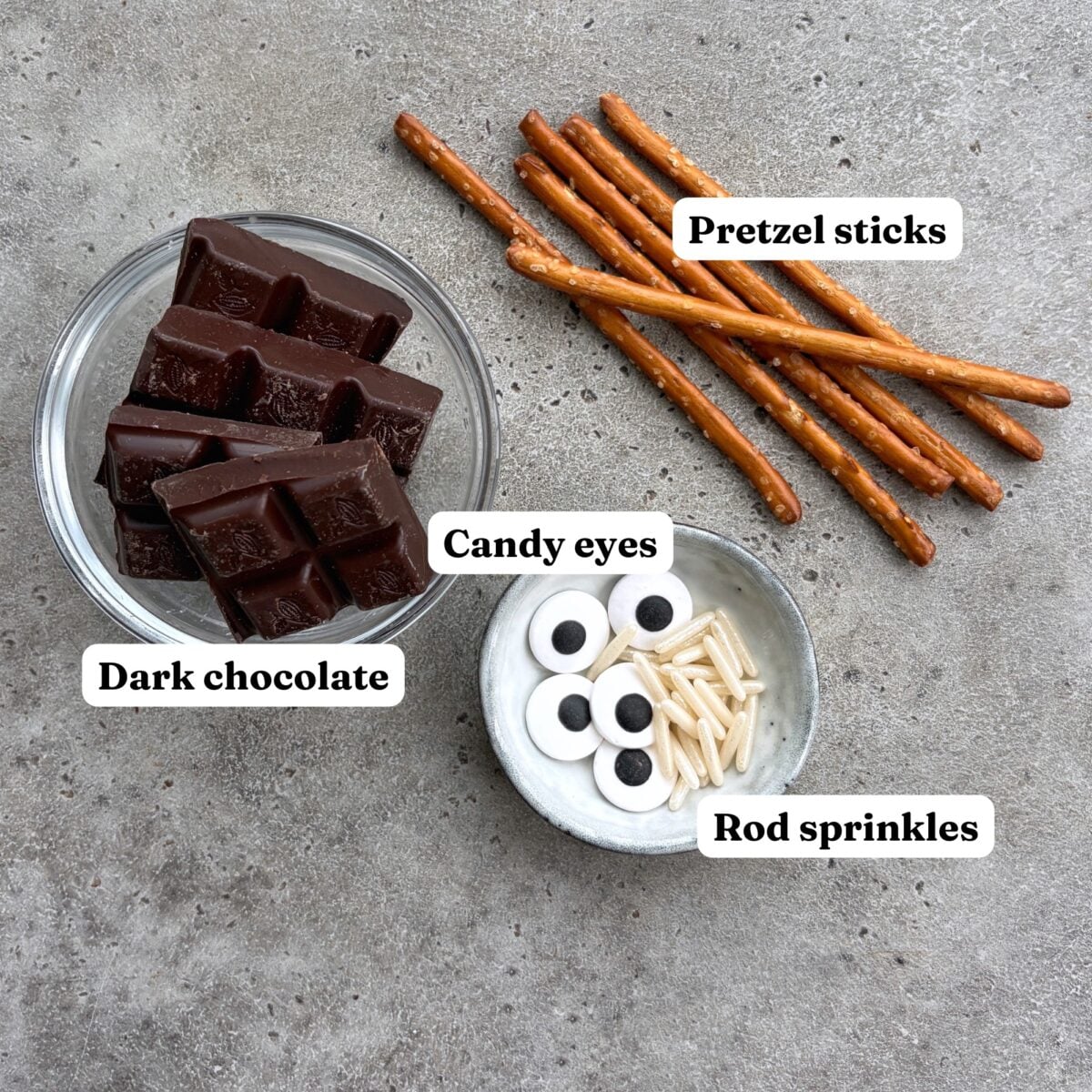Dark chocolate in a bowl, pretzel sticks, candy eyes, and rod sprinkles.