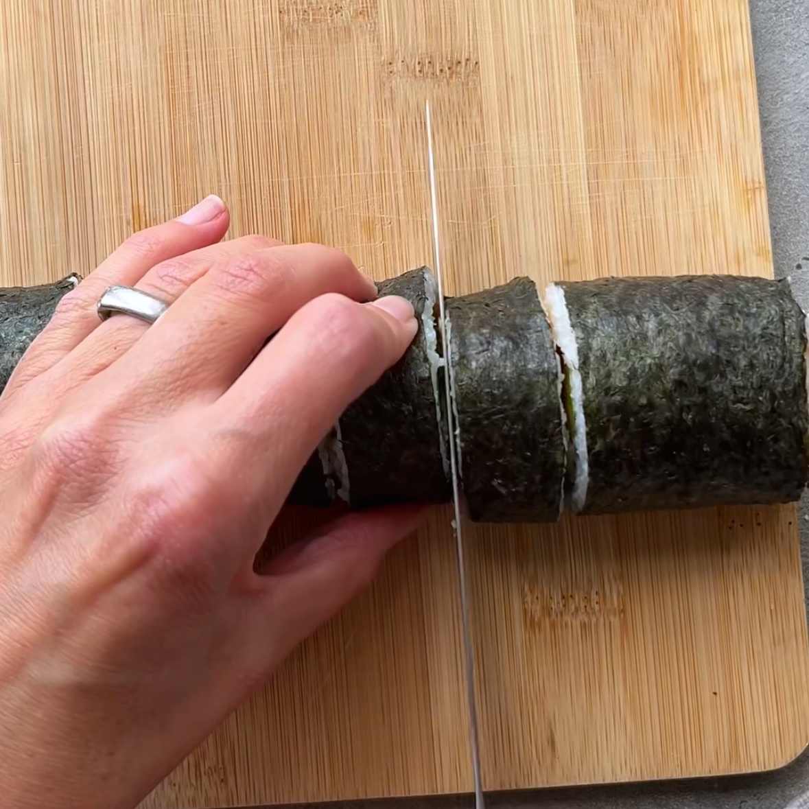 A hand is slicing a Halloween Sushi roll with a knife on a wooden cutting board.