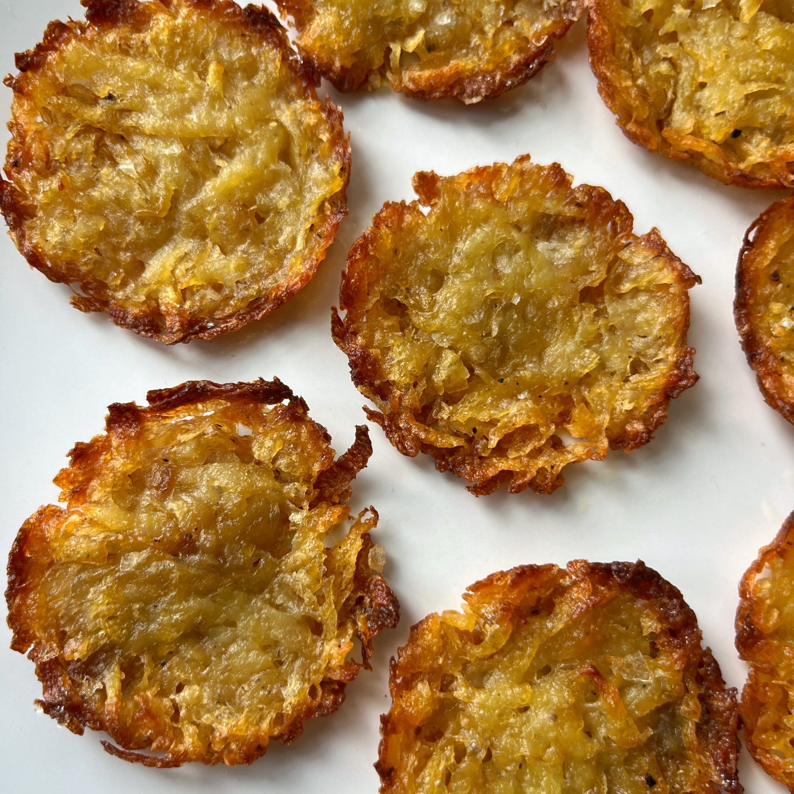 Close-up of several golden-brown Muffin Pan Potato Rosti with crispy edges and moist, textured centers, arranged on a white surface.