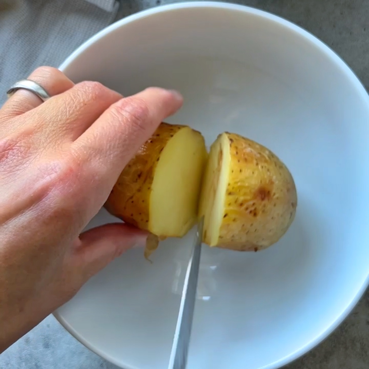 A hand holds a baked potato while a knife cuts it in half.
