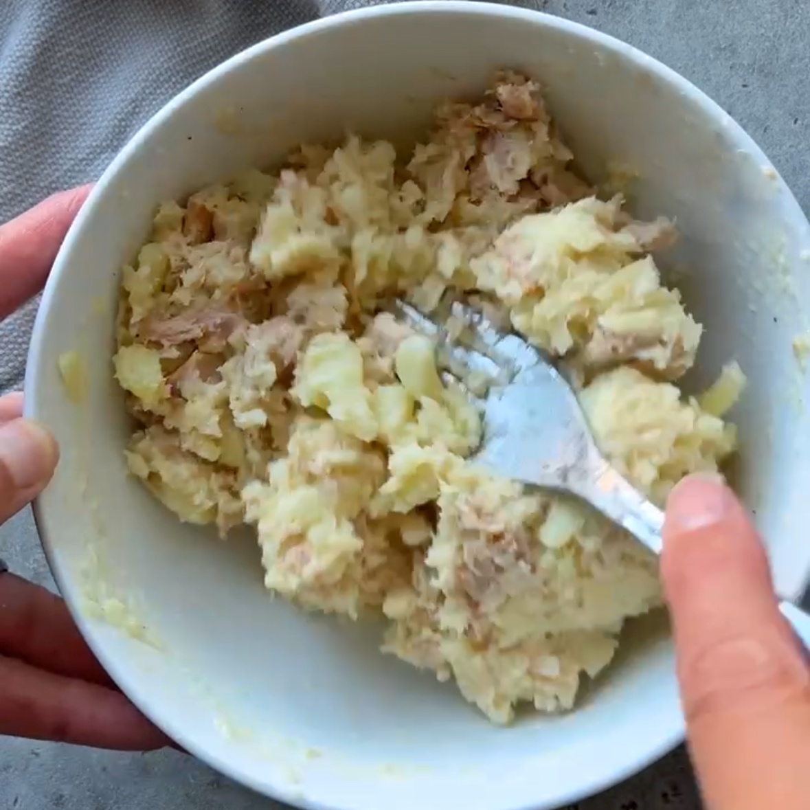 A fork mixes potato filling featuring tuna, butter, potato flesh, and cheese to top onto baked potatoes.