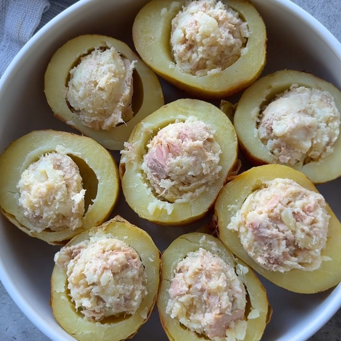 Halved baked potatoes are filled with a tuna, potato flesh, cheddar, and butter mixture.