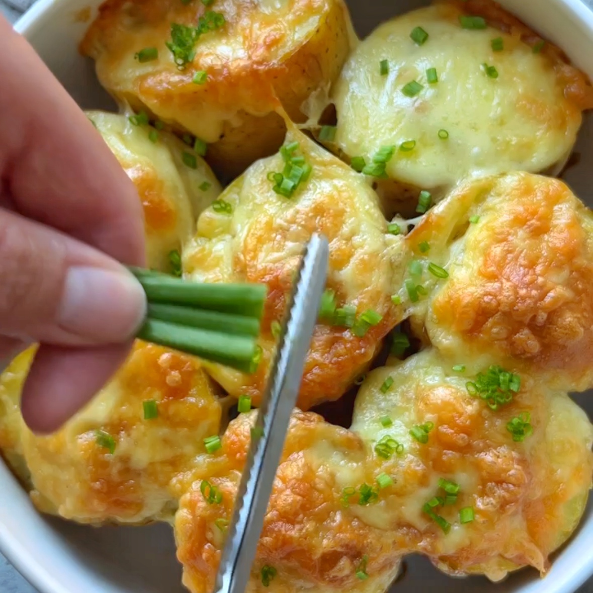 Scissors cut chives over freshly baked stuffed Baked potatoes.