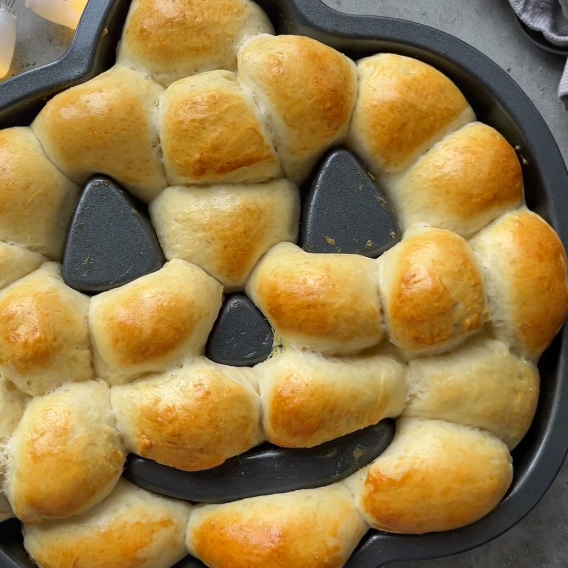 Halloween Bread rolls are baked and arranged in a pumpkin-shaped pan to resemble a festive jack-o’-lantern face.