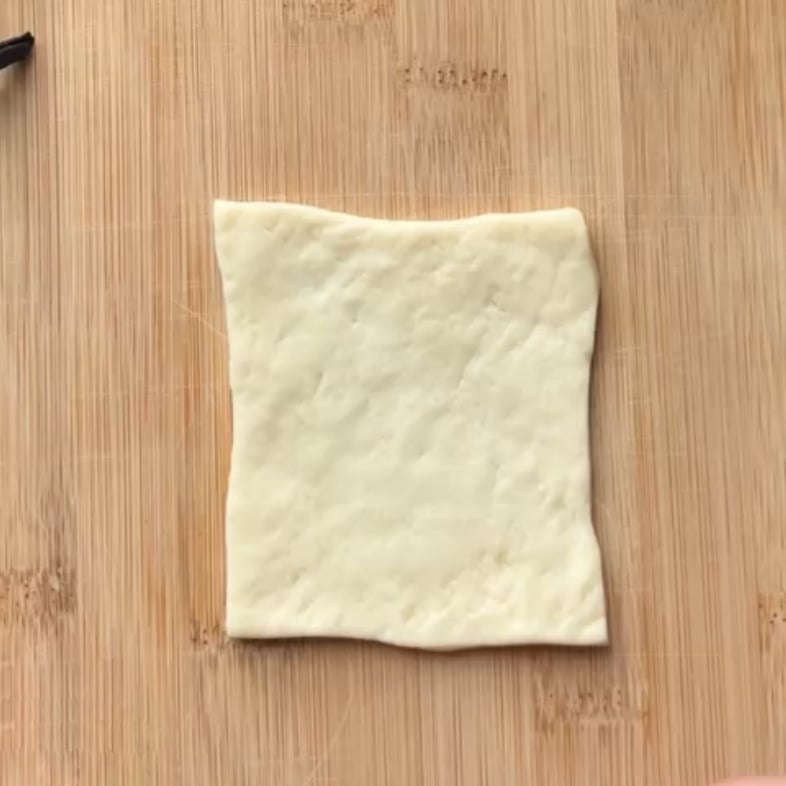 A rectangular piece of raw pizza dough sits on a wooden cutting board.