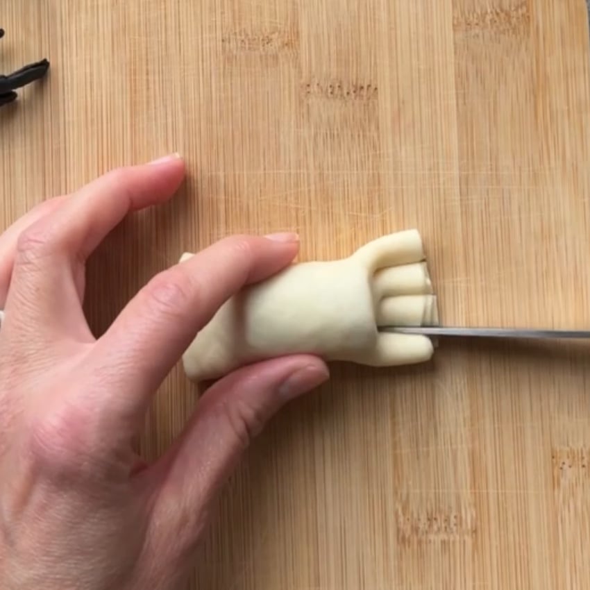 A hand uses a knife to cut lines into the dough on a wooden cutting board.