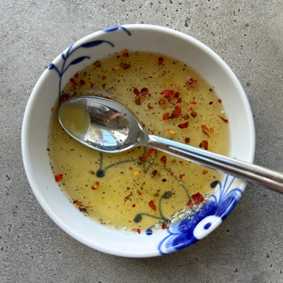 A spoon rests in a white and blue bowl filled with a sweet and sour dressing.