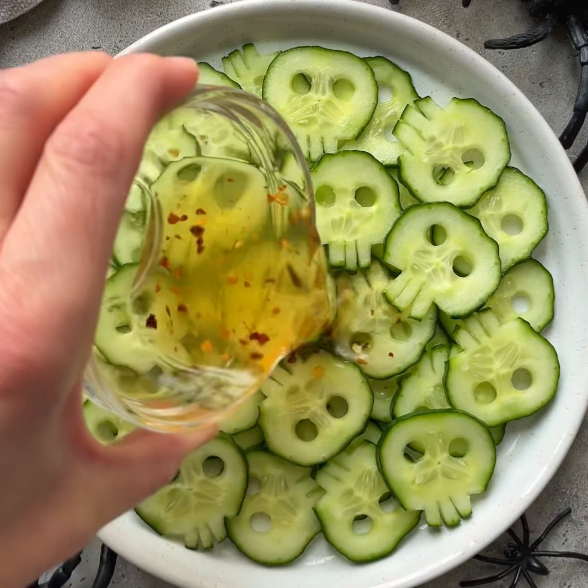 A hand pours a dressing on top of a cucumber skull salad.