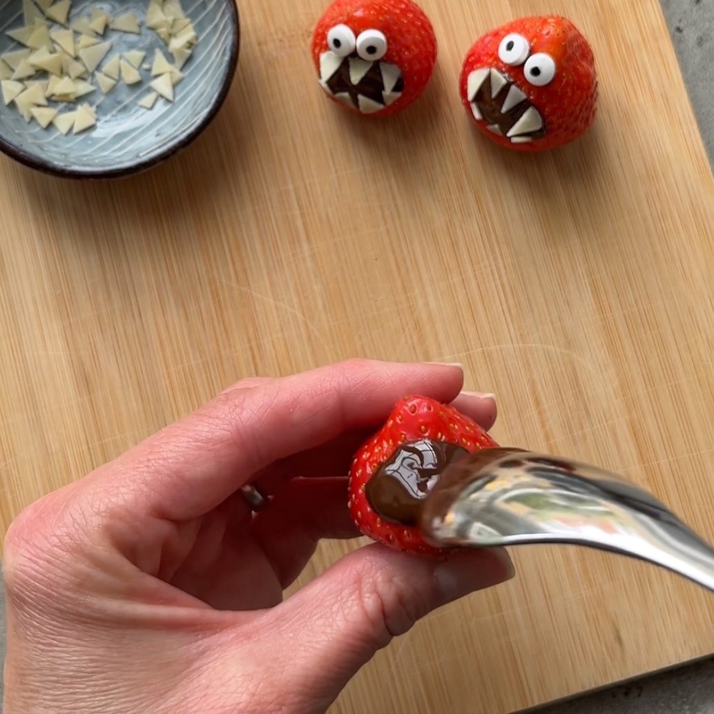 A hand spoons a chocolate mouth onto a strawberry.
