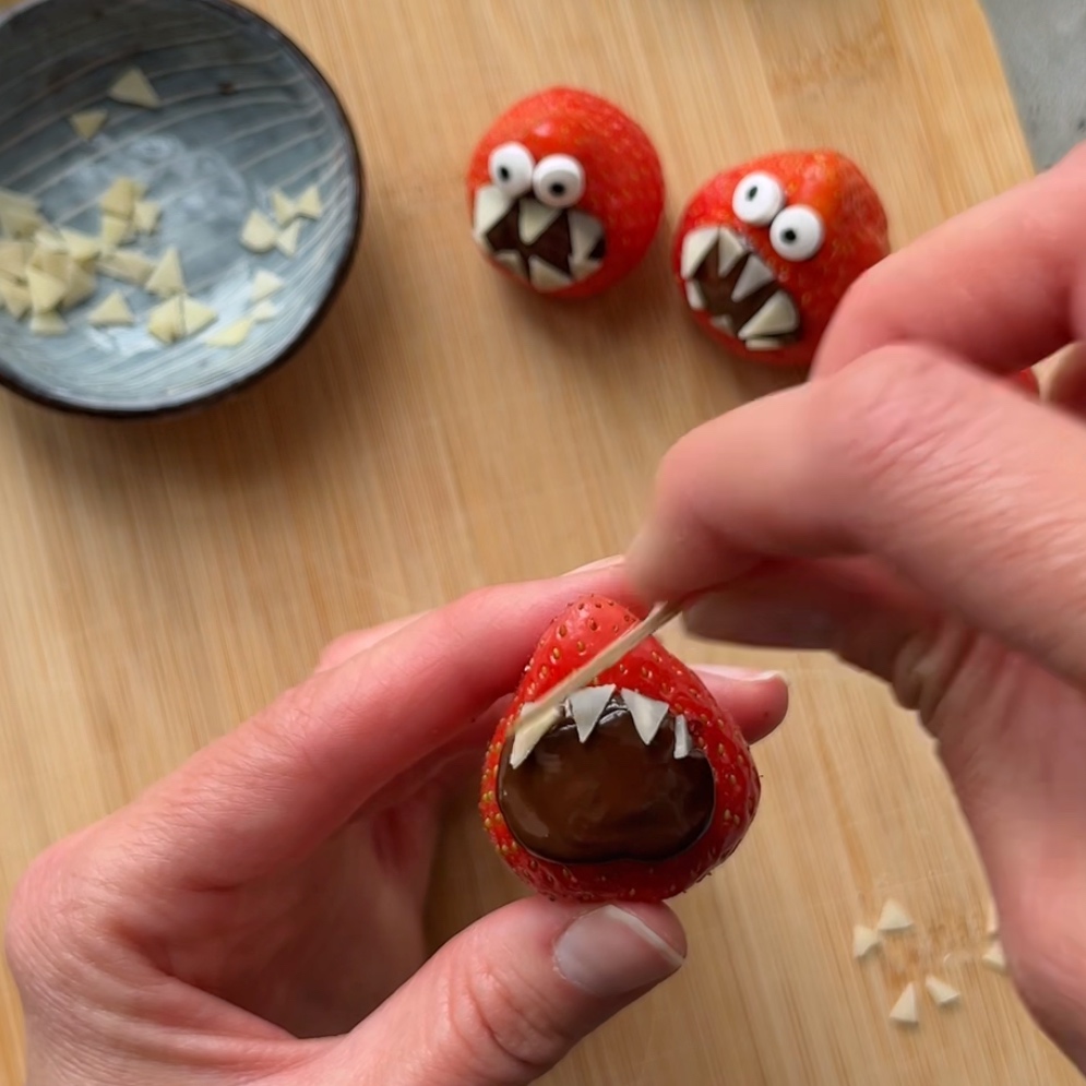 A toothpick arranges flaked almond teeth onto a strawberry.