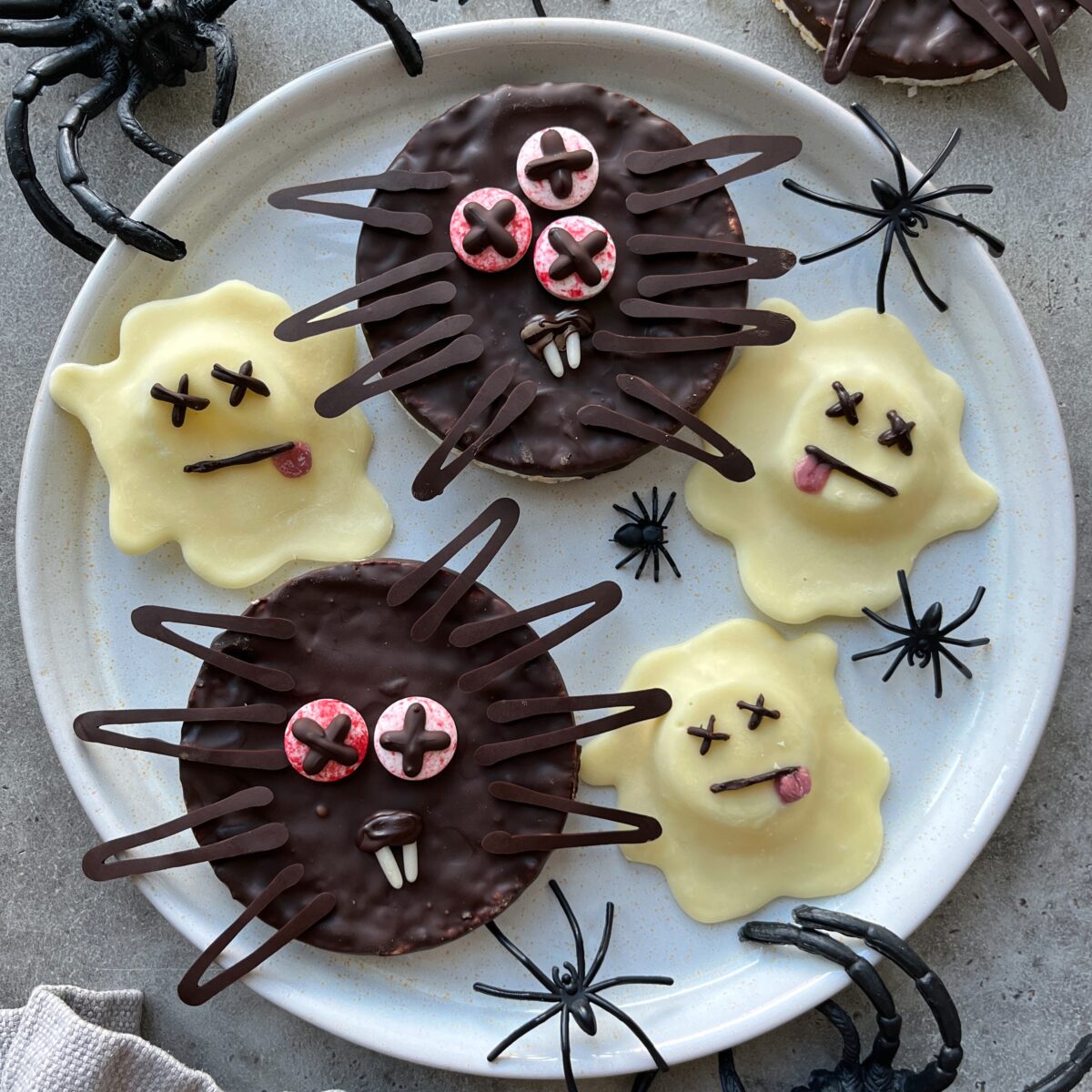 A plate of dark and white Halloween chocolates decorated as ghosts and dead spiders with candy eyes.