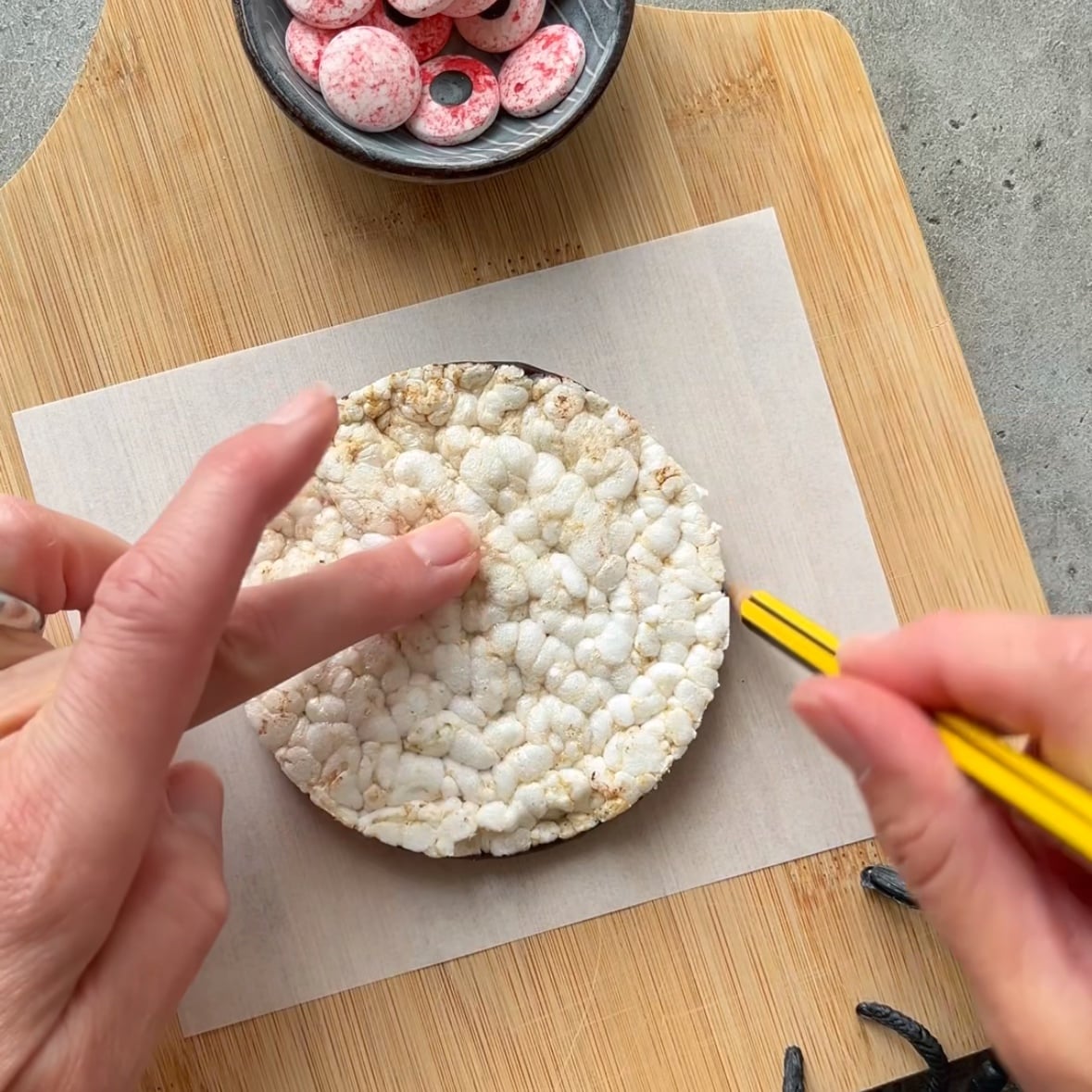 A person uses a yellow pencil to trace around a rice cake on parchment paper.