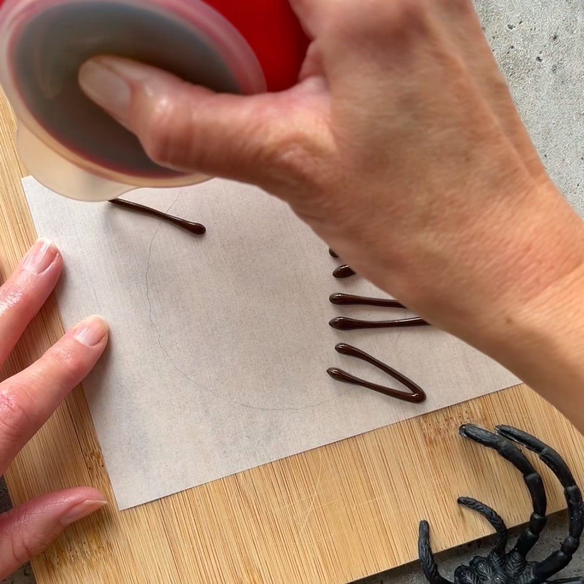 A person pipes chocolate onto parchment paper on a wooden board.