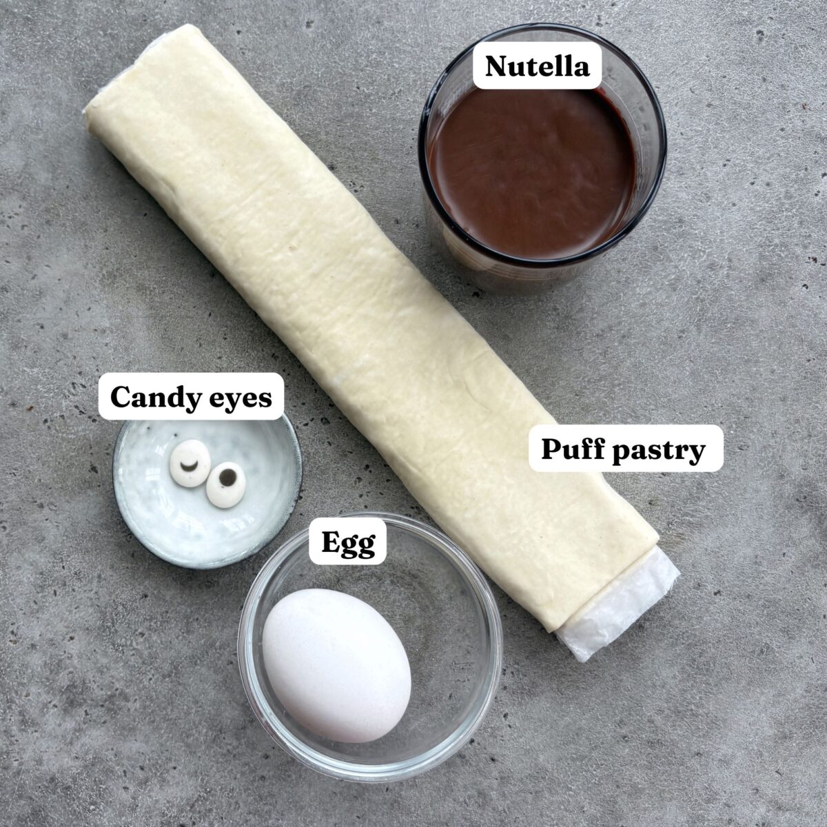 Sheets of puff pastry, a glass of Nutella, an egg, and two candy eyes.