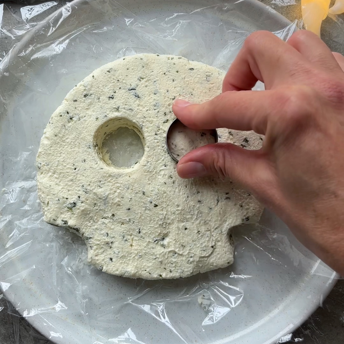 A hand cuts out an eye with a round cookie cutter.