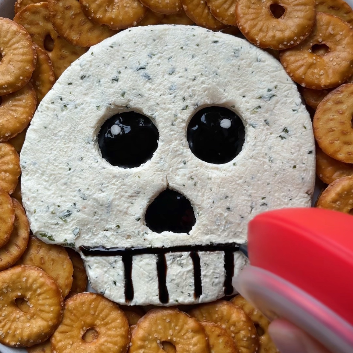 A piping utensil filled with balsamic glaze pips a dark trim outlining teeth on a skull. 