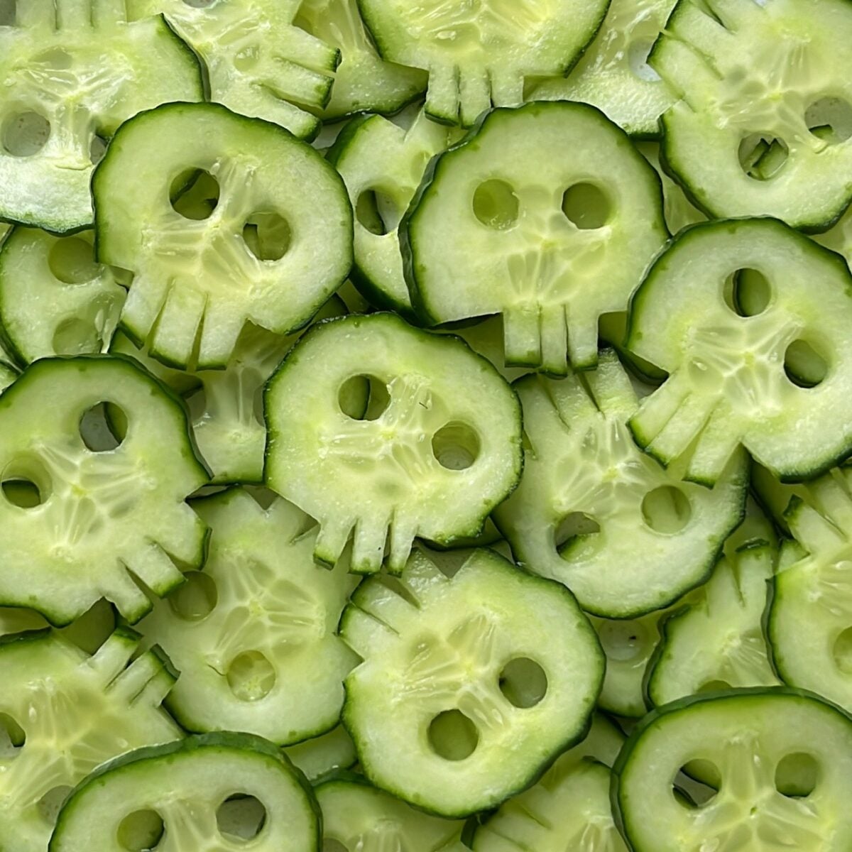 Cucumber slices carved into skull shapes, layered on top of each other to create a striking pattern.