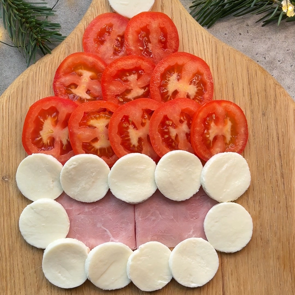 Assembling a Christmas caprese using ham slices for the face, tomato and mozzarella slices for the hat, and a mozzarella beard.