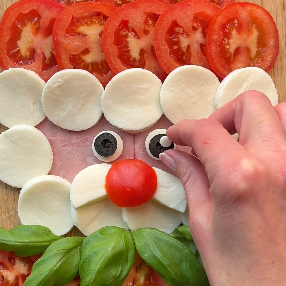 Adding final details to a Christmas Caprese featuring mozzarella and tomato slices, ham, and fresh basil.